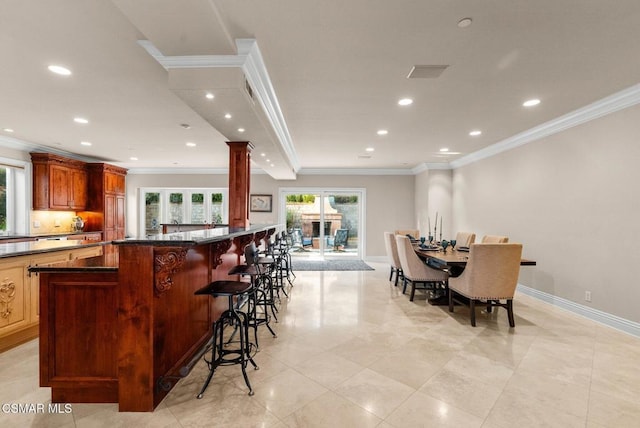 kitchen with dark stone countertops, ornamental molding, decorative columns, and a breakfast bar