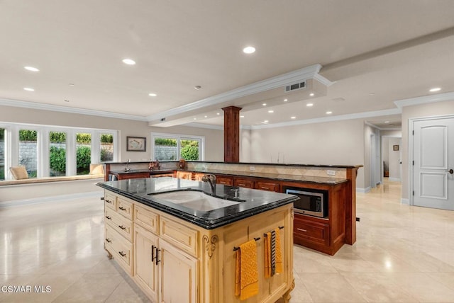 kitchen featuring stainless steel microwave, sink, dark stone countertops, ornamental molding, and a kitchen island with sink