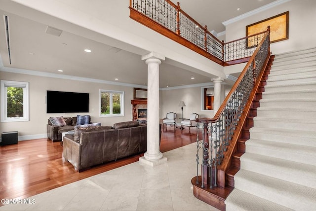 living room featuring crown molding, decorative columns, light hardwood / wood-style flooring, and a high ceiling