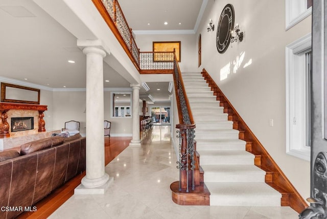 entrance foyer with ornate columns, ornamental molding, a high ceiling, and a fireplace