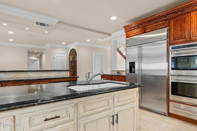 kitchen featuring sink, dark stone countertops, stainless steel appliances, tasteful backsplash, and cream cabinetry