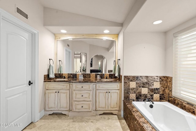 bathroom featuring lofted ceiling, vanity, a wealth of natural light, and tiled tub