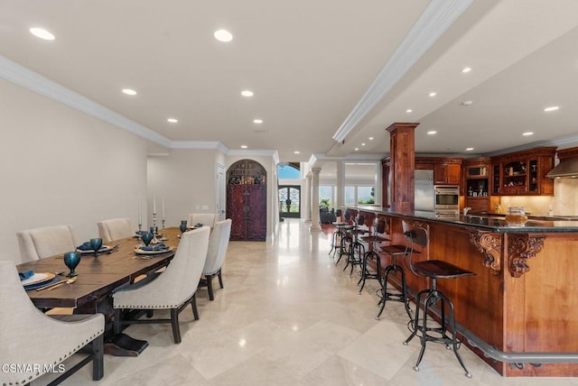 dining space with ornate columns, ornamental molding, and bar