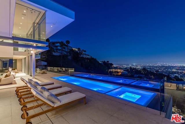 pool at twilight with an in ground hot tub and a patio area