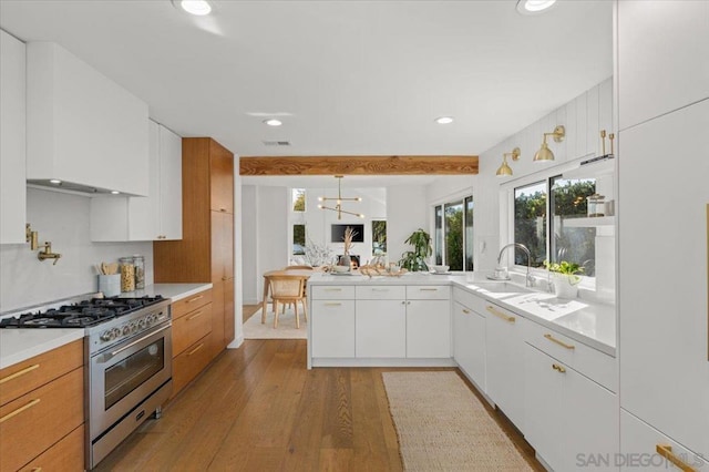 kitchen with pendant lighting, sink, white cabinets, stainless steel range, and light wood-type flooring