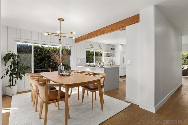 dining space with a notable chandelier, wood-type flooring, and beamed ceiling