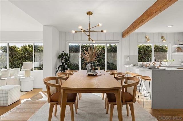 dining area with beam ceiling, a chandelier, and light hardwood / wood-style floors