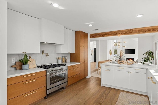 kitchen with pendant lighting, tasteful backsplash, white cabinets, high end stainless steel range, and light hardwood / wood-style flooring