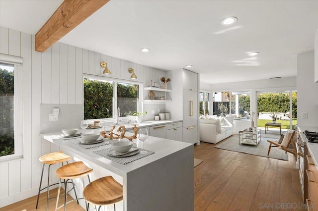 kitchen with hardwood / wood-style flooring, a breakfast bar, white cabinetry, beam ceiling, and kitchen peninsula