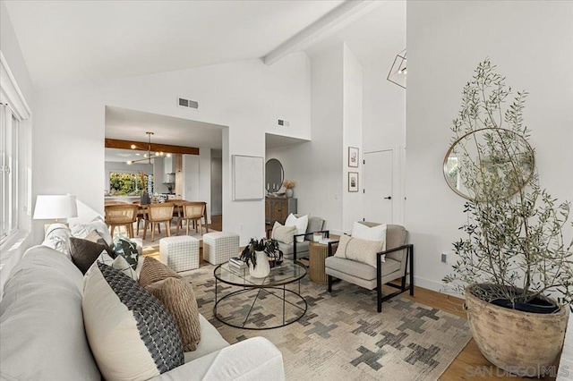 living room with beamed ceiling, a notable chandelier, high vaulted ceiling, and light wood-type flooring