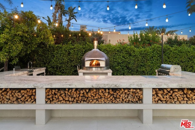 patio terrace at dusk featuring a grill, a fireplace, and exterior kitchen