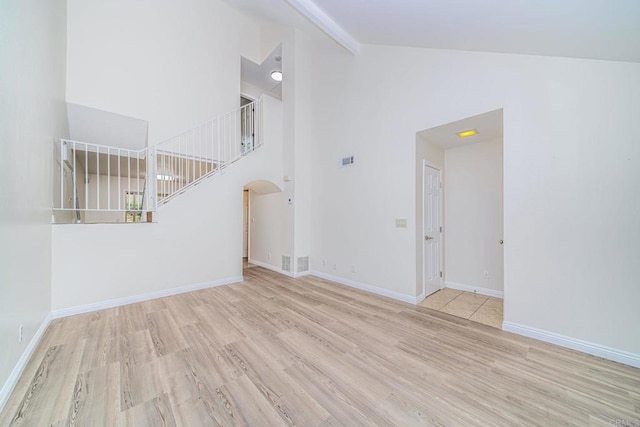 unfurnished room with arched walkways, high vaulted ceiling, baseboards, and wood finished floors