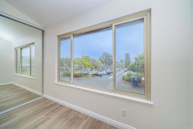 unfurnished room featuring plenty of natural light, baseboards, lofted ceiling, and light wood-style flooring