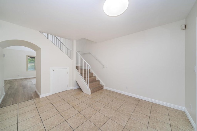 empty room featuring light tile patterned floors, arched walkways, baseboards, and stairway