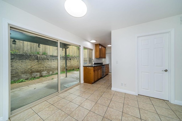 kitchen featuring light tile patterned floors, baseboards, stainless steel dishwasher, a sink, and brown cabinetry