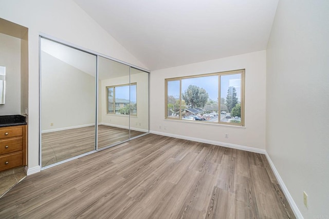 unfurnished bedroom featuring baseboards, lofted ceiling, light wood-style flooring, and a closet