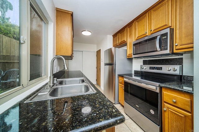 kitchen featuring brown cabinets, light tile patterned floors, a sink, and stainless steel appliances