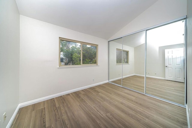 unfurnished bedroom featuring baseboards, wood finished floors, vaulted ceiling, and a closet