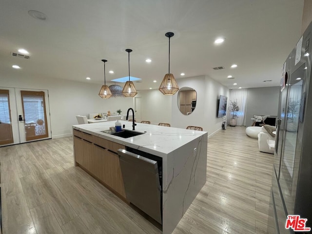 kitchen with sink, hanging light fixtures, a kitchen island with sink, stainless steel dishwasher, and light stone counters