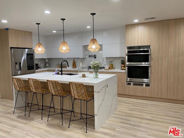 kitchen with appliances with stainless steel finishes, decorative light fixtures, white cabinetry, sink, and a spacious island