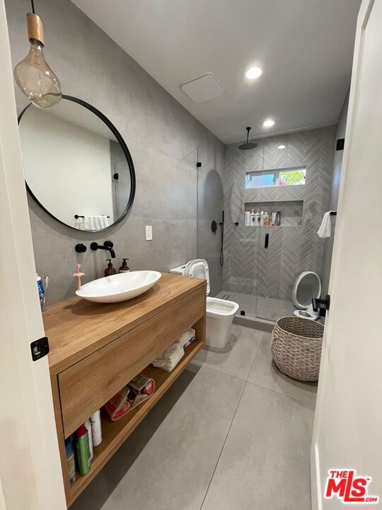 bathroom with tile patterned flooring, tile walls, vanity, a shower with shower door, and toilet