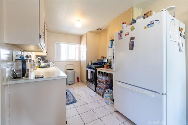 kitchen with white refrigerator, light tile patterned floors, sink, and stainless steel gas stove