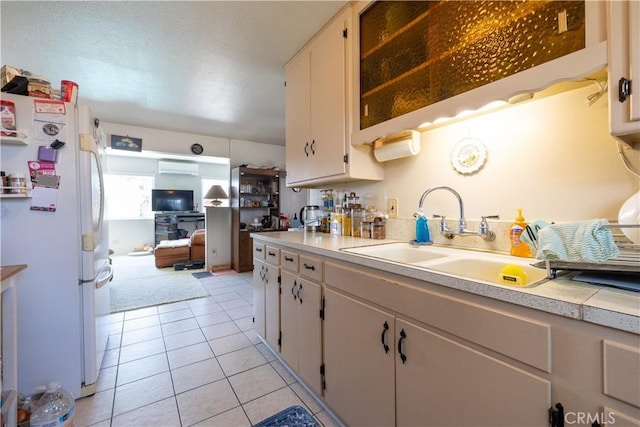 kitchen with sink, light tile patterned floors, a wall mounted AC, white refrigerator, and white cabinets