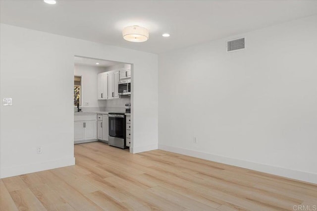 interior space featuring appliances with stainless steel finishes, light wood-type flooring, and white cabinets