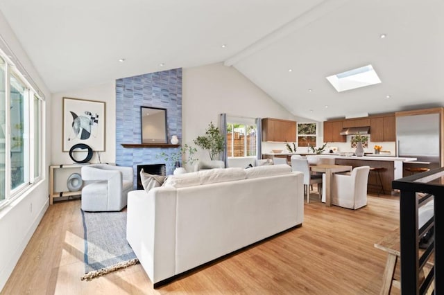 living room featuring light hardwood / wood-style flooring, a skylight, high vaulted ceiling, a large fireplace, and beamed ceiling