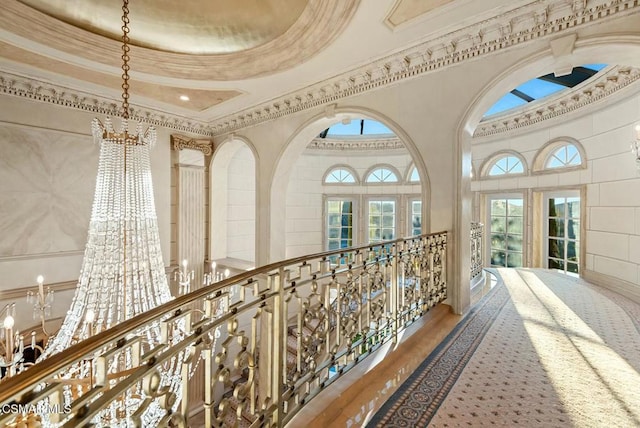 hall with ornamental molding, an inviting chandelier, and a tray ceiling