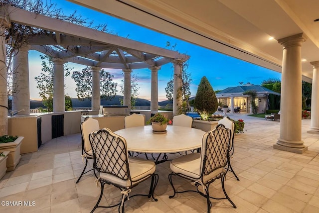 patio terrace at dusk featuring a pergola and exterior kitchen