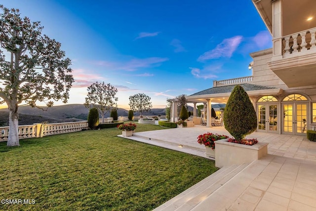 yard at dusk featuring french doors, a mountain view, and a patio area