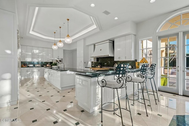 kitchen with custom exhaust hood, a tray ceiling, a kitchen island, pendant lighting, and white cabinets