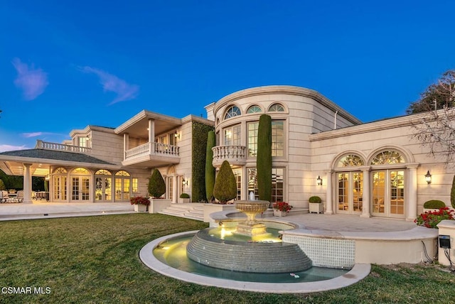 back house at dusk with french doors, a balcony, a yard, and a patio area