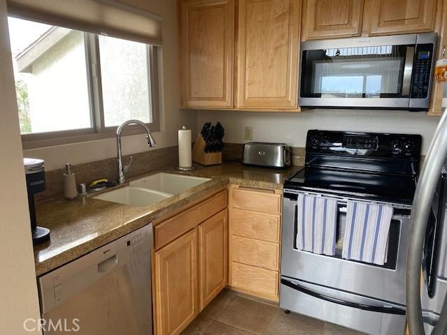 kitchen featuring tile patterned floors, appliances with stainless steel finishes, light brown cabinetry, and sink