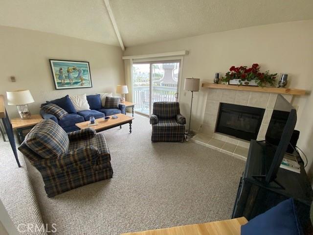 living room featuring carpet flooring, a fireplace, vaulted ceiling, and a textured ceiling