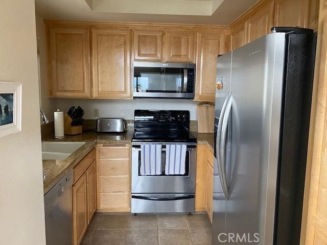 kitchen featuring appliances with stainless steel finishes, light brown cabinetry, sink, light stone countertops, and tile patterned floors