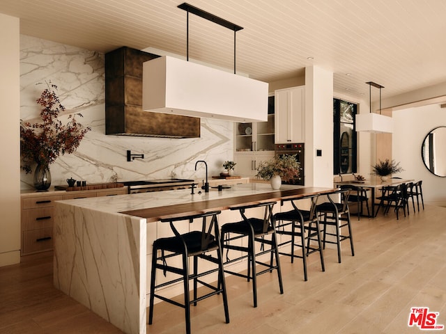 kitchen with hanging light fixtures, white cabinetry, a kitchen breakfast bar, and light wood-type flooring