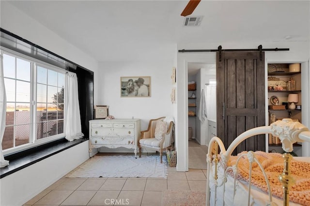 bedroom featuring light tile patterned floors, a barn door, and ceiling fan