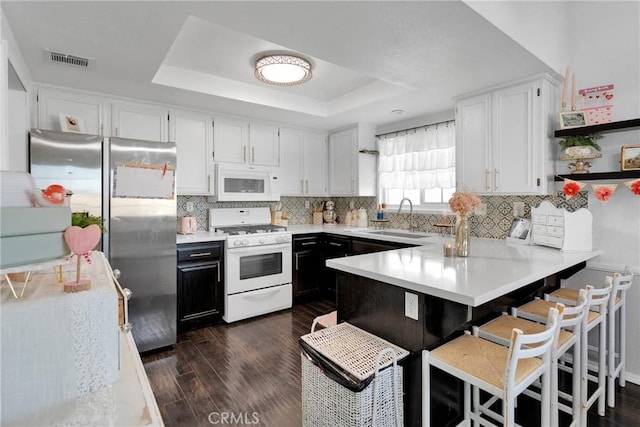 kitchen featuring sink, white appliances, backsplash, white cabinets, and a raised ceiling