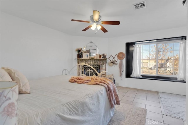 bedroom with a brick fireplace, ceiling fan, and light tile patterned flooring