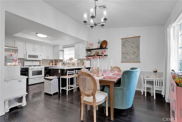 dining space with sink, a notable chandelier, dark hardwood / wood-style floors, and a raised ceiling