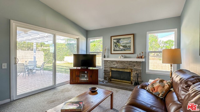 living room featuring a stone fireplace, vaulted ceiling, light carpet, and a wealth of natural light