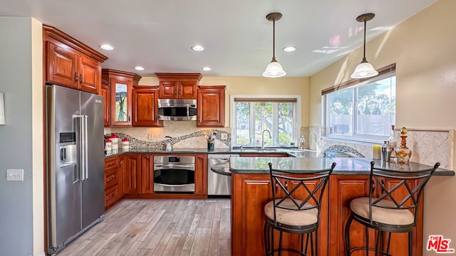 kitchen with appliances with stainless steel finishes, sink, a kitchen bar, hanging light fixtures, and kitchen peninsula