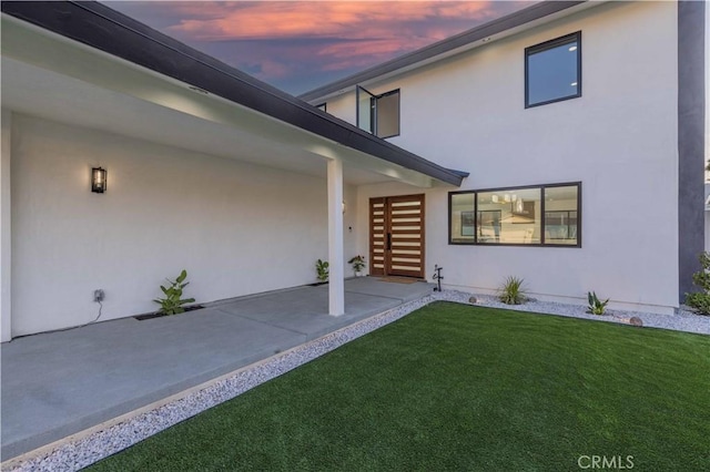 entrance to property featuring a patio, a yard, and stucco siding