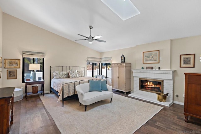 bedroom with a brick fireplace, dark hardwood / wood-style floors, vaulted ceiling with skylight, and ceiling fan