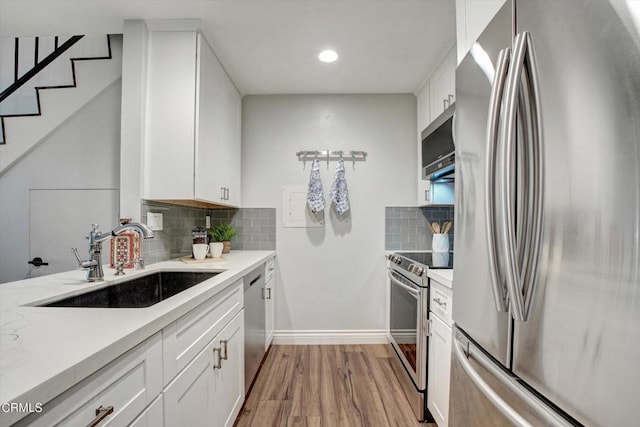 kitchen with appliances with stainless steel finishes, sink, white cabinets, and light hardwood / wood-style floors