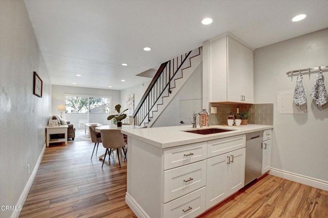 kitchen featuring dishwasher, sink, white cabinets, kitchen peninsula, and light hardwood / wood-style flooring