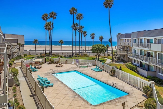 view of swimming pool with a water view, a beach view, and a patio area