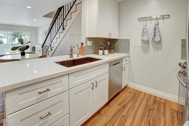 kitchen with sink, white cabinetry, stainless steel dishwasher, kitchen peninsula, and light wood-type flooring